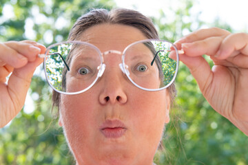 glasses with thin metal frame in female hands, funny female face, Vision Impairment and Its Impact,...