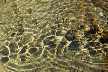 Abstract patterns under the surface of water on rock river bottom from ripples in sunny weather.