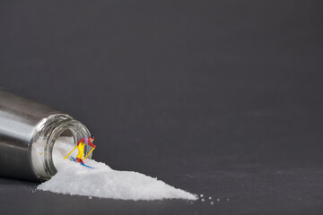 Photography of miniature people and toy figures, a skier rides down a mountain of salt from a salt shaker, dark background
​