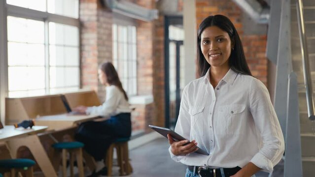Portrait of smiling young businesswoman holding digital tablet working in modern open plan office turning to look at camera - shot in slow motion