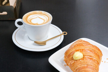 A cappuccino, croissant with vanilla cream on a black table on a cafe 