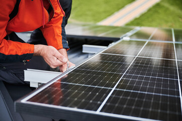 Man technician mounting photovoltaic solar panels on roof of house. Close up view of engineer...