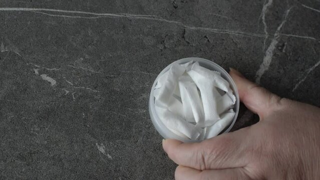 A woman opens a box of nicotine snus. takes one pad and places it on the gray stone table.