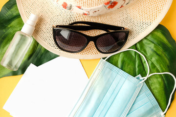 Straw hat, sunglasses and face medical mask on yellow background. Top view. Travel during the...