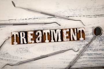 TREATMENT Concept. Alphabet blocks and dental tools on a white wooden background