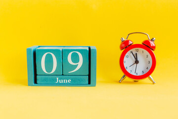 June 9. Blue cube calendar with month date and alarm clock on bright yellow background