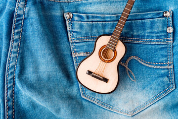 Toy acoustic guitar on blue jeans background, top view
