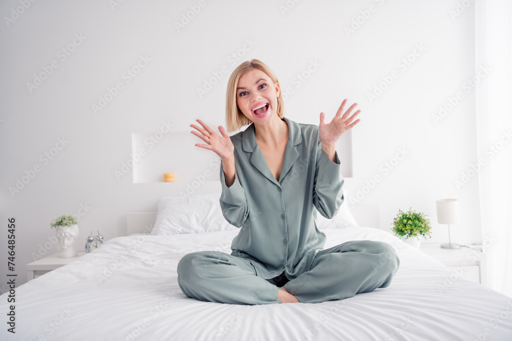 Poster Photo of young barefoot girl wearing cute grey pajama have some fun in bedroom sitting on bed raised arms up indoors light white interior