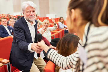 Speaker giving microphone to male audience during business session