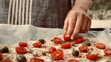 Woman preparing traditional Italian focaccia puts cherry tomatoes on top of the dough. Cooking...
