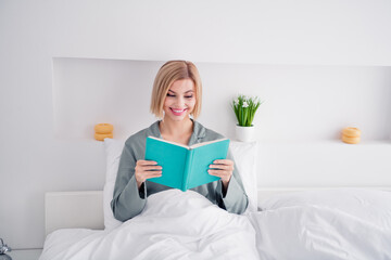 Photo portrait of blonde attractive young woman sit bed read book wear trendy gray pajama light...