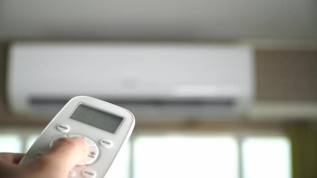 Man's hand using remote control open The air conditioner is cooled to 25 degrees Celsius in his bedroom.
