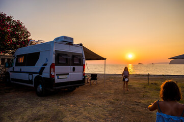 Campervan is parked on the beach at sunset.