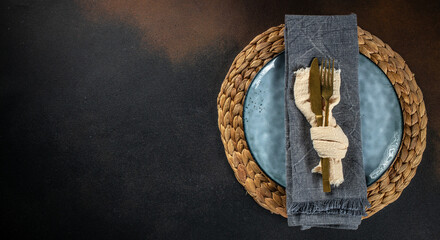 Table setting with blue plate, cutlery and napkin on dark concrete background for restaurant or...