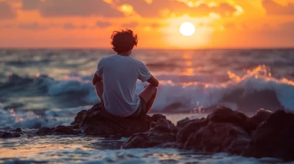Foto op Canvas A man sitting on a rock at the ocean watching sunset, AI © Alexandr