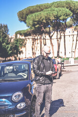 Happy smiling bearded man standing near a car at Rome,Italy.Man holding a mobile phone standing outdoors next to his car texting ,sending parking sms