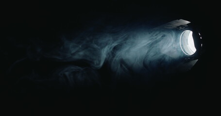 In the dark, a robust directional light source beams through, revealing fog swirling in its path