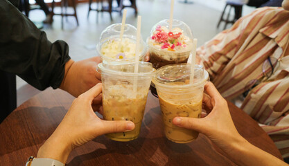 Group of hands holding glass of ice coffee together at cafe.