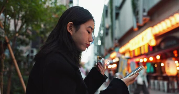 Phone, eating and Japanese woman with onigiri in Tokyo city on exploring vacation, adventure or holiday. Hungry, food and young female person enjoying an Asian snack or meal in town on weekend trip.