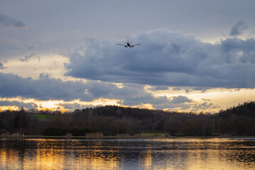 Obraz na płótnie Canvas Samolot lecący nad zbiornikiem wodnym / jeziorem na tle zachodzącego słońca | The flying plane above the reservoir / lake on the sunset background
