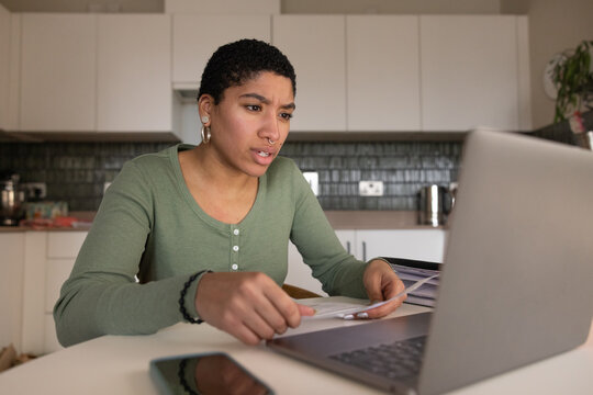 Young adult female at home looking at bills and personal finances using a laptop computer