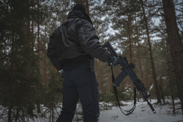 A private military man with an AK 12 rifle in the forest in winter, view from the back.
