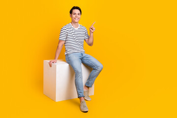 Full length photo of cute good mood guy dressed striped t-shirt sitting podium pointing empty space...