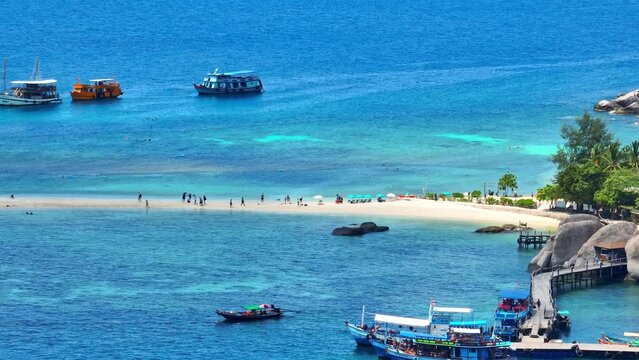A lively sandbar packed with sightseers, enveloped by boats on tranquil turquoise waters, an idyllic spot for sun-soaked adventures. Drone aerial view. Koh Nangyuan, Thailand. Tropical background. 4K.