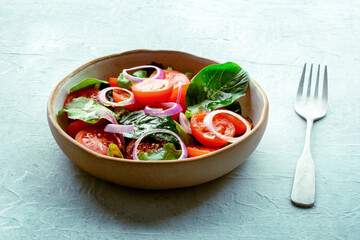 Salad with tomato, fresh leaves, and onions, on a slate background, with a fork. Healthy diet, simple vegan recipe - 746527070