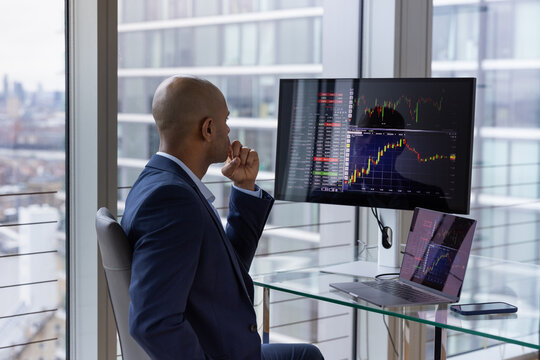 Stock trader looking at stocks and shares on computer in a high rise office