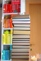 High stack of books on the table. Colorful rainbow bookshelf in the background. Selective focus.