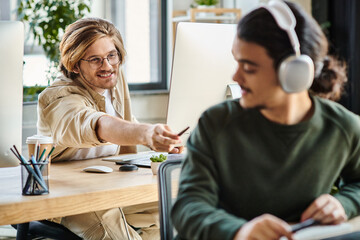 cheerful male professional in glasses passing his stylus pen to blurred coworker in headphones