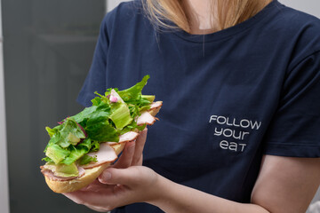 Kobieta na diecie je kanapkę z wędliną i duża ilością zielonej sałaty 