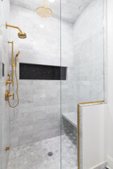 A walk-in shower with marble subway and hexagon tiles, a black hexagon niche shelf, and gold fixtures.