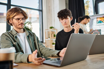Obraz premium Young startup team deeply focused while working on laptops in modern coworking space, men in 20s