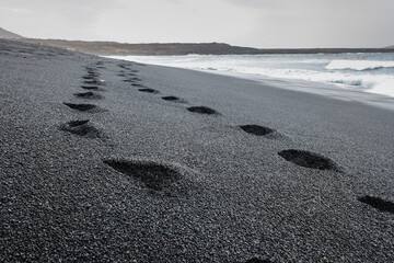 impronte sulla sabbia nera del vulcano dell'oceano  - obrazy, fototapety, plakaty