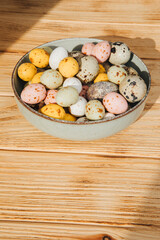 Multi-colored chocolate decorative eggs and quail eggs in green plate on a wooden background. Happy Easter background. Top view