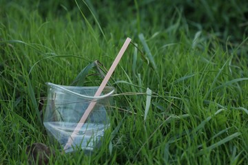 Used plastic cup with straw on grass outdoors, space for text. Environmental pollution concept