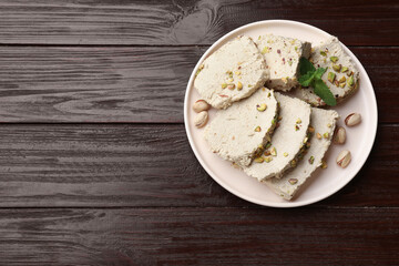 Pieces of tasty halva with pistachios and mint on wooden table, top view. Space for text