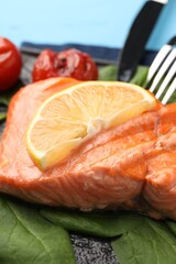 Tasty grilled salmon with tomatoes, spinach and lemon on table, closeup