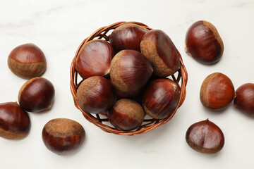 Obraz premium Sweet fresh edible chestnuts in wicker bowl on white table, top view