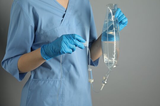 Nurse with IV infusion set on grey background, closeup