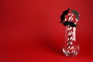 Fake paper mustaches and party props in glass on red background. Space for text