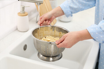 Woman rinsing pasta in colander above sink, closeup