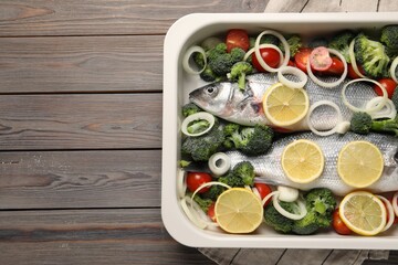 Raw fish with vegetables and lemon in baking dish on wooden table, top view. Space for text