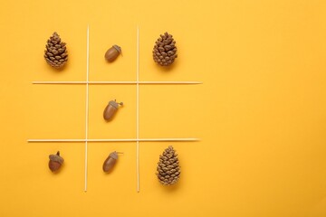 Tic tac toe game made with acorns and pine cones on yellow background, top view. Space for text