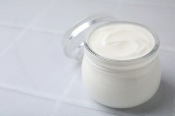 Fototapeta na wymiar Delicious natural yogurt in glass jar on white tiled table, closeup. Space for text