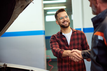 A smiling male owner of the car doing a handshake with his mechanic, at the car repair service.