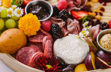 Cheese board served with fruits, vegetables, ham, crackers, sweets. Plate of cheese and snacks on wooden board for restaurant, menu, advert or package, close up selective focus