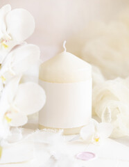 Fototapeta na wymiar Pillar candle with a blank label near white orchid flowers close up, pastel romantic mockup